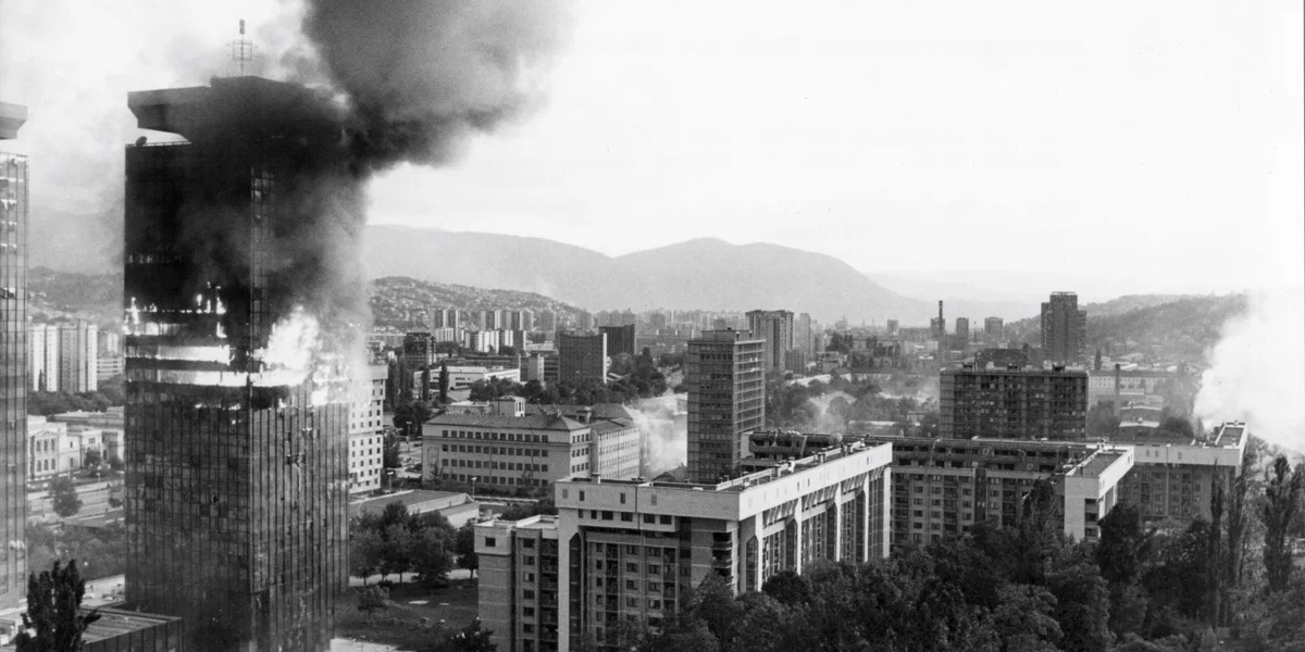 Ee vun den Tierm vun der Firma UNIS am Zentrum vu Sarajevo brennt no Ugrëff vun der serbescher Arméi am Juni 1992. Déi zwee Tierm, déi ëmmer nees bombardéiert goufen, hu sech am Verlaf vum Krich zu Symboler vum Duerchhalverméigen vun der Stad entwéckelt | © picture alliance / dpa | Gobet